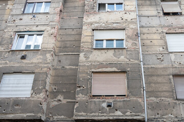a wall of the building that bears the scars of war. The many bullet holes and destroyed plaster create a powerful reminder of the war events and their impact on the urban environment.