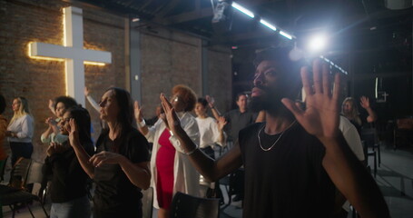 Diverse congregation raising hands in worship during church service, illuminated cross in background, spiritual connection and collective devotion in sacred space