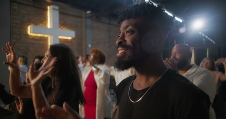 Multicultural congregation clapping and smiling during church worship, illuminated cross in background, expressions of faith, joy, unity, and spiritual devotion