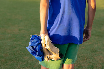 Young soccer player holding shoes and clothes while walking off the field after the game