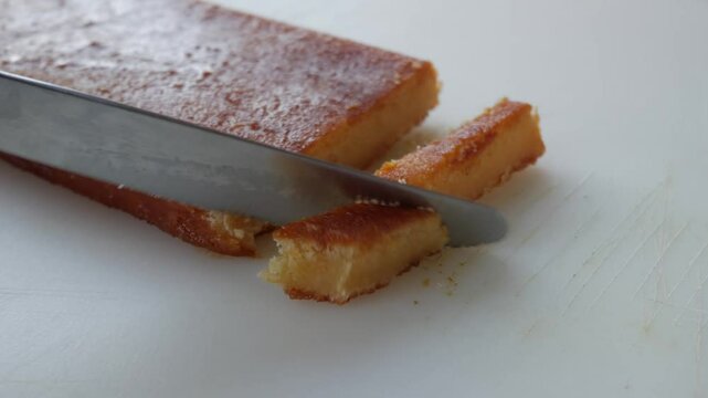 Sliced toasted egg yolk turron on a white cutting board with a knife