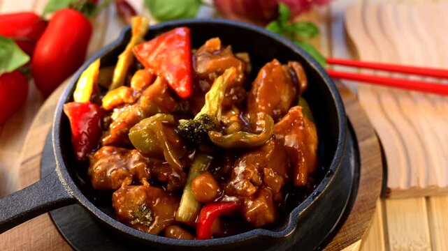 Cast iron skillet holding sizzling chicken cashew stir fry, garnished with cherry tomatoes, garlic, basil leaves, red chopsticks resting on rustic wooden surface