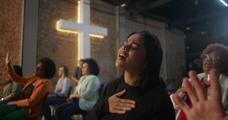 Women singing in prayer during church service, one raising hand in worship while another holds...