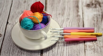 A cup and a saucer with clews balls of yarn wool and crocheted blanket handmade craft bright photo	