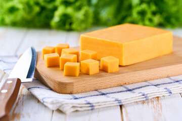 cutting board with red cheddar cheese cubes on white kitchen table, selective focus.