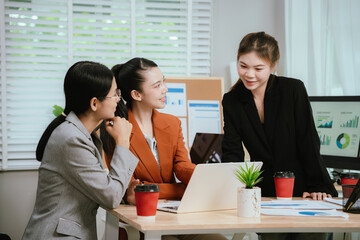 Asian business team collaborating in office, discussing strategy and project planning; professional men and women using laptop during brainstorming meeting.