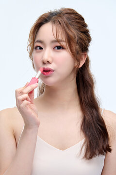 Young Asian Woman in Sleeveless Top Holding Makeup Tool Against White Background