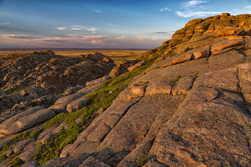 on top of a mountain overlooking the steppe under the sunset sky. Layered rocks. Beautiful summer landscape at sunset