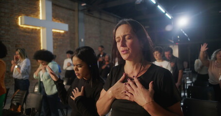 Diverse group in deep worship, hands on heart, glowing cross in background, collective spiritual connection, heartfelt faith, and unity in sacred church gathering