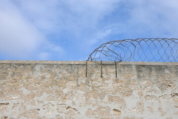 High sandstone prison wall, with razor wire on top, blue sky. Background concept. Copy space. Crime, felony, legal system, conviction rate, justice, sentencing, escapees. Youth crime statistics.
