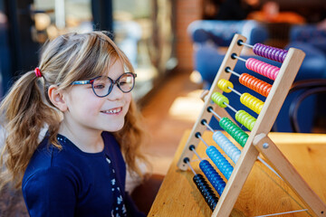 Little preschool girl playing with educational wooden rainbow toy counter abacus. Healthy happy child with glasses learning to count and colors, indoors on sunny day.