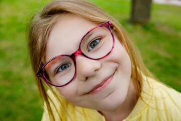 Portrait of a happy smiling school girl with eyeglasses in a sunny park. Cute and cheerful child...
