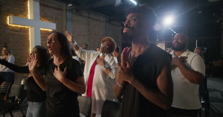 Diverse congregation in worship, hands over heart and raised in praise, glowing cross in background, collective spiritual connection, unity, and faith in sacred church service