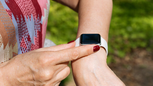 Close-up of a woman using a smartwatch with a white strap in a green forest, tracking activity or checking notifications during an outdoor walk.