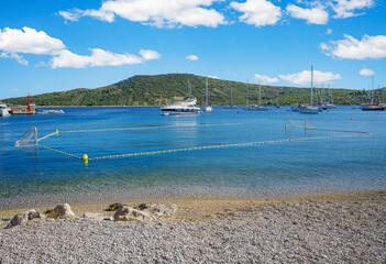 Obraz premium A tranquil coastal scene featuring clear turquoise waters, anchored yachts, and a green hillside under a bright blue sky in Primosten, Croatia.