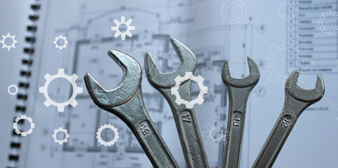 Bunch Of Wrenches above Blurred Paper Draw and White Silhouettes of Cogs and Gears on a Foreground
