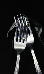 Silvery identical forks linked together isolated on black backdrop 
