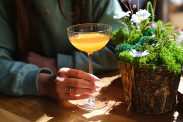 Woman holding cocktail glass. Elegant orange drink in hand. Refreshing beverage on wooden table....