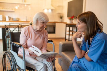 Care assistant with her elderly patient enjoying reading and looking happy