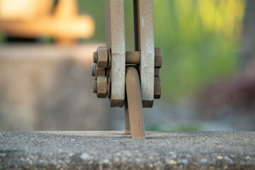 Double metal bar connection to lug embedded in concrete. Connection is made with three bolts with nuts. Green and yellow background.  Abstract, conceptual.