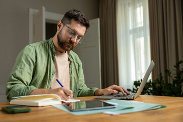 Bearded man taking notes on laptop in home office