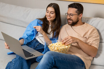 Woman and her boyfriend watching movie on laptop while eating junk popcorn