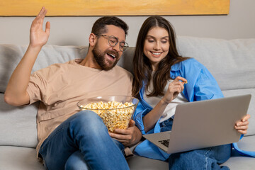 Couple enjoying cozy evening at home watching movie together with popcorn on sofa