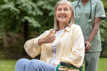 Woman on a wheelchair feeling wonderful while having a walk in the park with a nurse