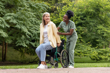 African american nurse rolling a wheelchair of female patient in the park