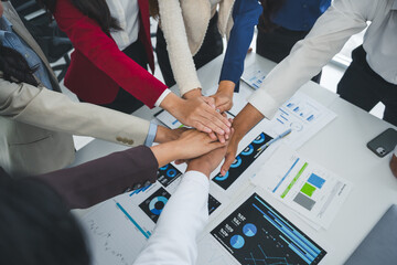 Business people stacking hands together showing teamwork and unity in achieving goals during a corporate meeting analyzing financial charts