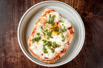 A delicious homemade pizza with melted mozzarella cheese, tomato sauce, and fresh parsley on a white plate, placed on a rustic wooden table. Perfectly baked, appetizing, and ready to enjoy