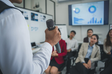 Businessman holding microphone making a speech to his colleagues during a meeting in the office