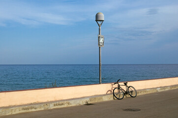 bicycle leaning on wall in front of the sea, Finale Ligure, Liguria, Italy