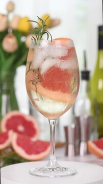 Grapefruit Prosecco Gin Spritz cocktail, combining tart grapefruit, gin and sparkling prosecco with a sprig of rosemary. Vertical video, real time, circular motion