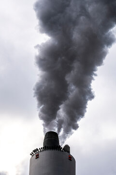 Thick black smoke column billowing from cylindrical chimney, captured from low angle with texture detail, symbolizing heavy industry and air contamination.