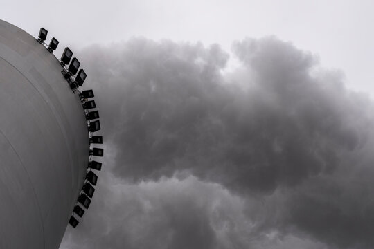Side view of large industrial smokestack releasing heavy black smoke, highlighting air pollution and fossil-based energy production in moody light.