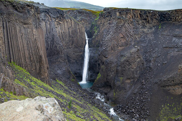 Powerful Studlafoss waterfall plunging through dramatic basalt columns and dark volcanic cliffs in...