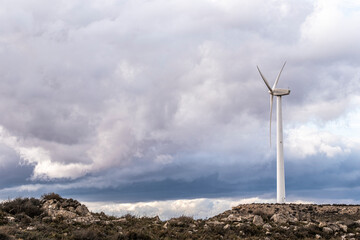 Lone turbine framed by dramatic weather and rocks in rural Zaragoza landscape, with open sky perfect for text overlay in clean compositions.