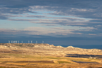 Distant view of wind turbines across dry hills under layered sky in Zaragoza, with clear copy space and renewable energy visual for clean tech content.