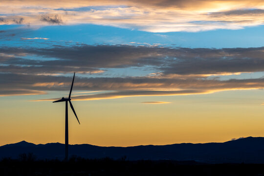 Wind turbine silhouette at dusk with vibrant sky colors and horizon in Zaragoza, Spain, suitable for sustainability visuals with copy space available.