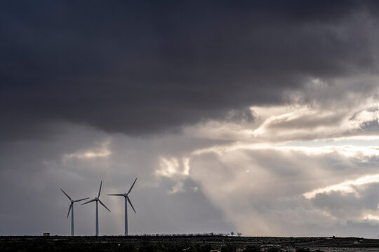 Silhouetted turbines under moody sky with visible beams of light breaking through, captured in Zaragoza with environmental and editorial use in mind.