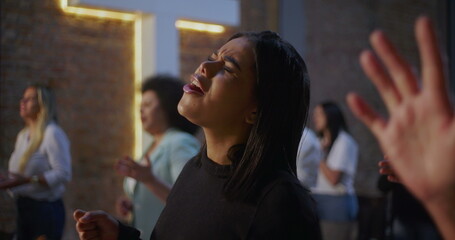Young woman singing in worship with outstretched hand, expressing faith and devotion in church setting with illuminated cross, emotional spiritual connection