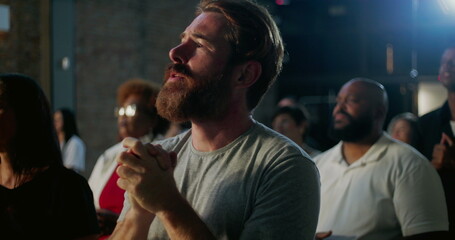 Man deeply immersed in prayer during spiritual worship, holding hands together, expressing devotion and faith alongside a diverse group in a church setting