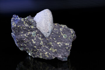 Natural agate gem stone in melaphyre with green amygdules on a dark shiny background. Nodule of uncut gemstone in basalt extrusive volcanic igneous rock. Mineral from northeast Czechia near Nova Paka.