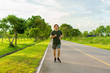 Sports man running on road for outdoor workout with warm light of sunset on freshy green background in rainy season. Jogging in nature. Healthy lifestyle.