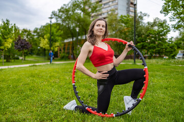 A girl in a red tank top and sweatpants does exercises and acrobatic tricks with a hula hoop on a...