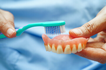 Asian senior woman patient clean teeth denture with toothbrush for chew food.