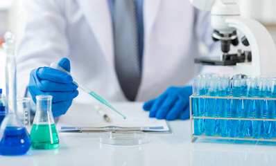 Scientist analyzing samples with pipette in laboratory. Scientist wearing blue gloves is holding a pipette with blue liquid over a petri dish, conducting research in a laboratory setting.