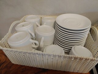 Clean and ready to use set of cups and saucers in the white basket 