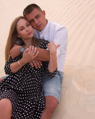romantic couple relationship. man and woman are sitting casual on a sand dunes career background in hugs and looking away with smile in desert at sunset. lifestyle concept, free space